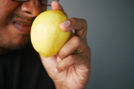 Man examining a yellow lemon in a close-up setting indoorsの写真素材