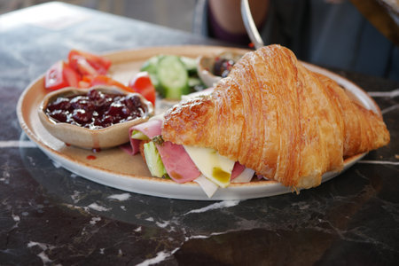 Delicious croissant sandwich served with fresh vegetables and jamの写真素材