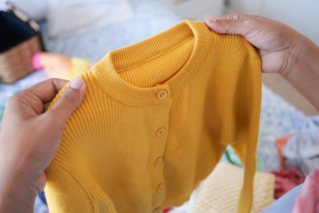 Hands grasp a yellow cardigan amid a colorful assortment of clothingの写真素材