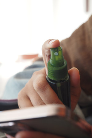 Mist spray bottle held by a person with a smartphone in viewの写真素材