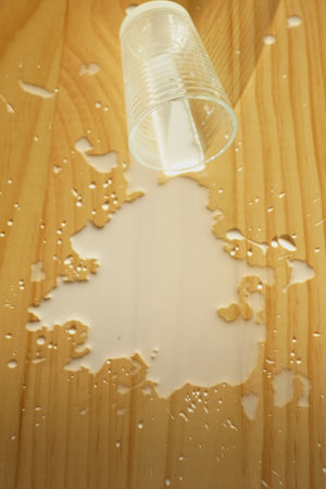 milk spilled on wooden surface with a plastic cup resting nearbyの写真素材