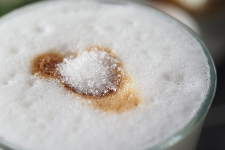 Coffee drink topped with sugar and foam in a cozy settingの写真素材