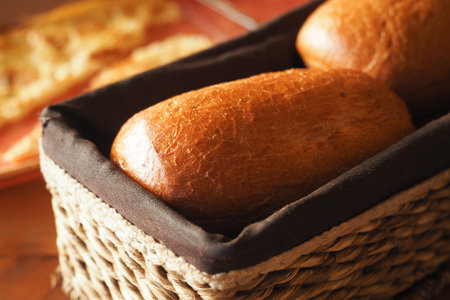 Freshly baked bread rolls in a woven basket on a wooden tableの写真素材