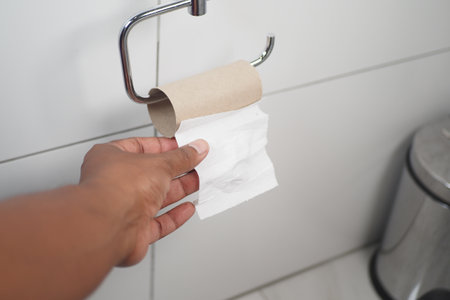Hand reaching for toilet paper in a modern bathroom settingの写真素材