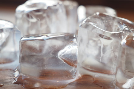 Melting ice cubes on a wooden surface reflecting light playfullyの写真素材