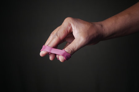 Close-Up of Hand with Pink Finger Exercise Tool Against Dark Backgroundの写真素材