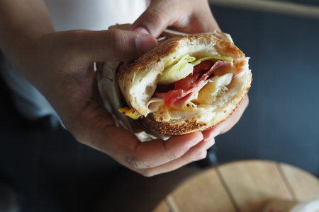 Delicious sandwich held by a person in a cozy cafe settingの写真素材