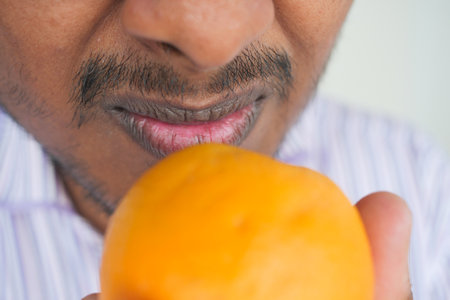 Man closely examines a ripe orange in a bright settingの写真素材