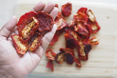 Dried tomatoes being held in hand over a wooden chopping boardの写真素材