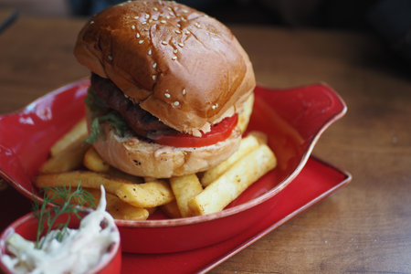 Delicious hamburger with fries served on a vibrant red plateの写真素材