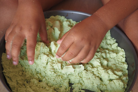 Child playing with green sand in a tray during a sunny afternoonの写真素材