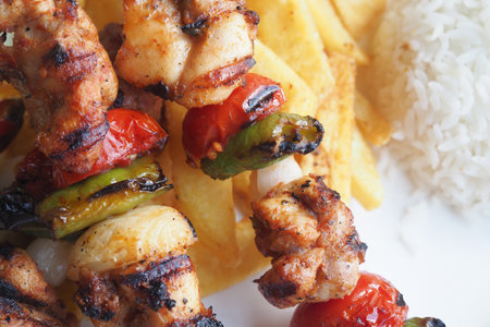 Grilled chicken skewers with rice and fries at a barbecueの写真素材