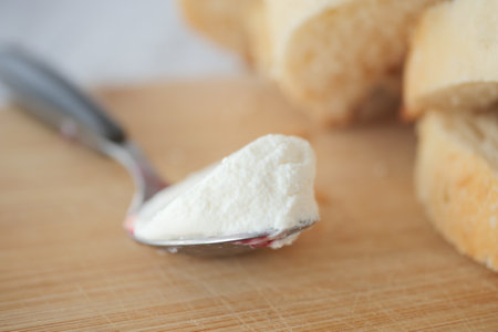 Fresh spread of creamy cheese on a spoon beside sliced breadの写真素材