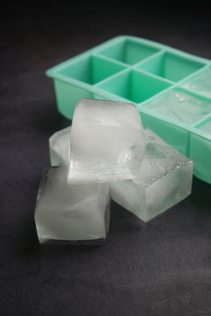 Ice cubes in various sizes beside a mint green ice trayの写真素材