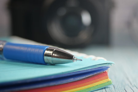 Colorful notebook and pen on a wooden surface with a camera backdropの写真素材