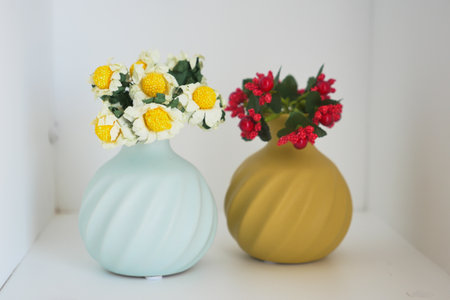 Colorful vases with flowers displayed on a shelf in a bright roomの写真素材