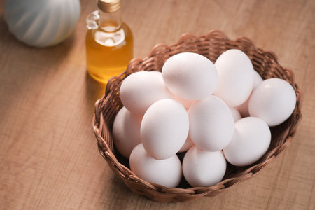 Fresh white eggs in a woven basket with cooking oil on a kitchen tableの写真素材
