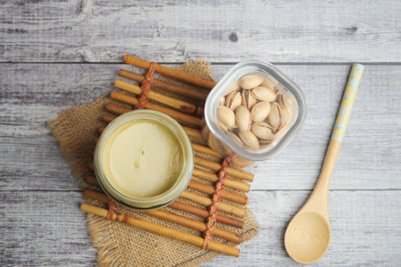 Creamy nut spread beside pistachios and wooden spoon on a tableの写真素材