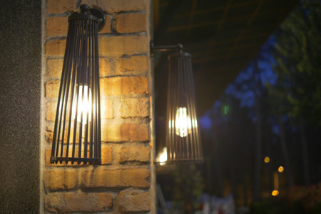 Rustic outdoor lamps illuminate a brick wall at dusk in a cozy settingの写真素材