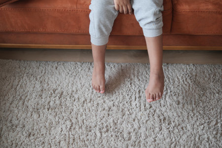 Child sitting on a couch with bare feet on a soft rugの写真素材