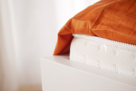 Cozy bedding view featuring an orange blanket and white mattressの写真素材