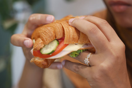 Croissant sandwich with fresh vegetables being enjoyed in a cafeの写真素材