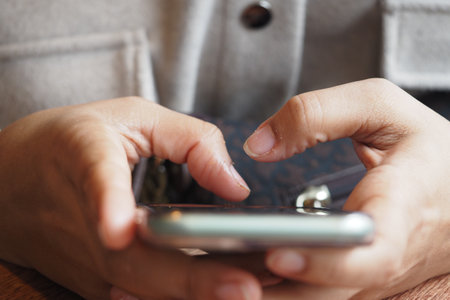 Person using smartphone while sitting at wooden tableの写真素材