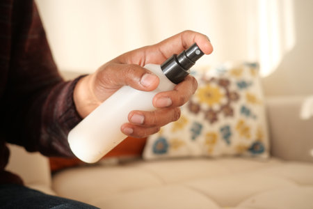 Close-Up of Hand Spraying Cleaner on Upholstered Sofa in Living Roomの写真素材