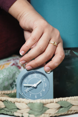 Hand adjusting clock on bedside table in cozy settingの写真素材