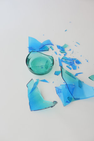 Shattered turquoise glass scattered on a white surfaceの写真素材