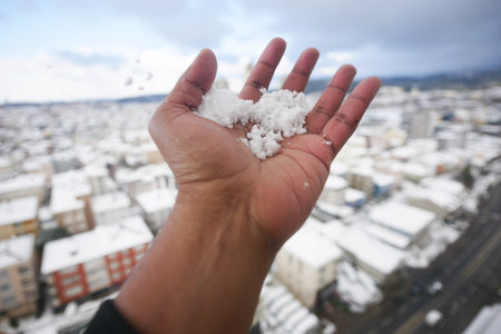 Snowy hand holds fresh snow over a winter city landscapeの写真素材