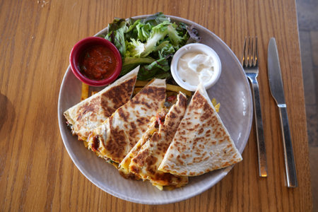Quesadilla served with fresh salad and dipping sauces at a restaurantの写真素材