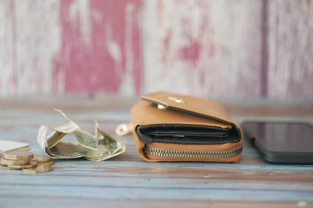 Wallet with cash and coins on wooden table near smartphone