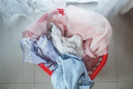 Laundry basket filled with colorful clothes on tiled floorの写真素材