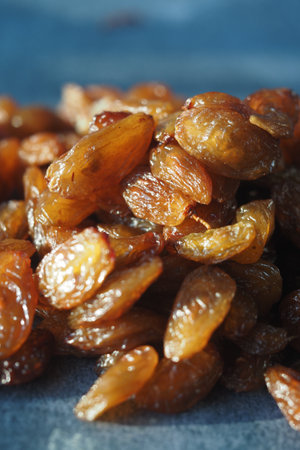 Dried golden raisins piled on blue surface during natural lightの写真素材