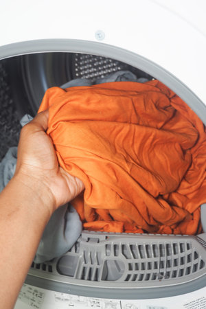 Colorful laundry being placed in a washing machine during daytime