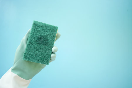 Cleaning sponge held by gloved hand against a blue backgroundの写真素材