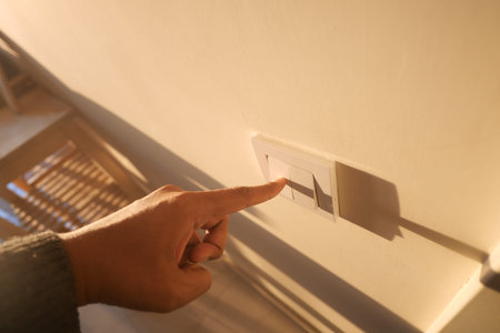 Hand pressing light switch on wall in a bright room at sunset