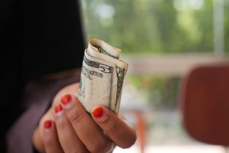 Hand holding a folded twenty-dollar bill in bright lighting