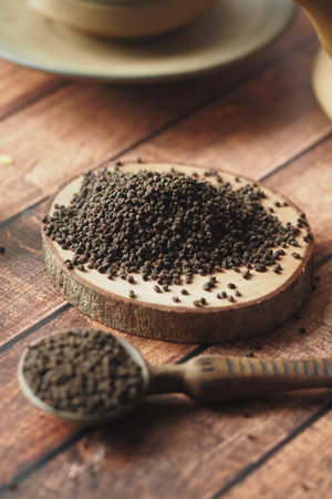 Black tea leaves displayed on wood with spoon and cup in backgroundの写真素材