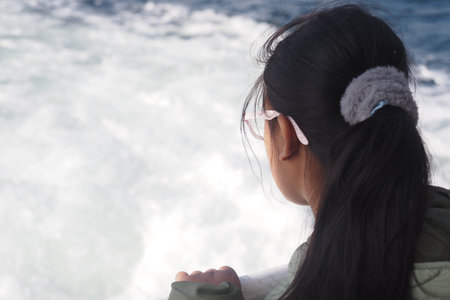 A girl gazes thoughtfully at the waves while enjoying a boat rideの写真素材