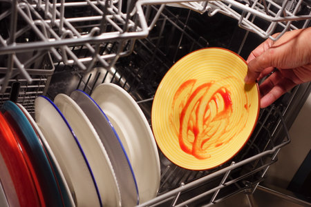 Cleaning dirty dishes in a dishwasher during evening hoursの写真素材