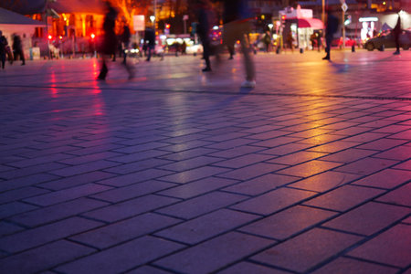 People walking on illuminated pavement in urban setting at nightの写真素材