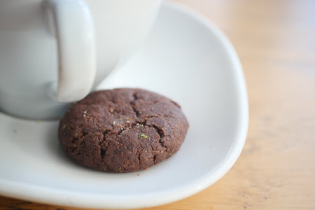 Warm chocolate cookie beside a cup on wooden tableの写真素材