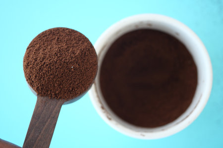 Ground coffee in measuring spoon over container on blue surfaceの写真素材
