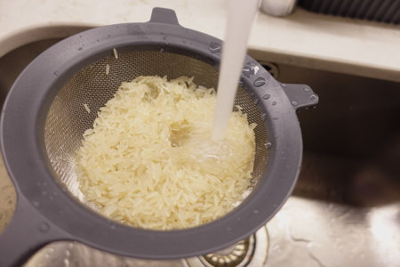 Cooking rice by rinsing it in a colander over a sinkの写真素材
