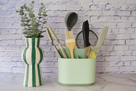 Kitchen tools arranged in pastel container with decorative plantの写真素材