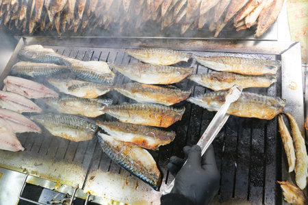 Grilling fresh fish on a smoky outdoor barbecue at a lively marketの写真素材