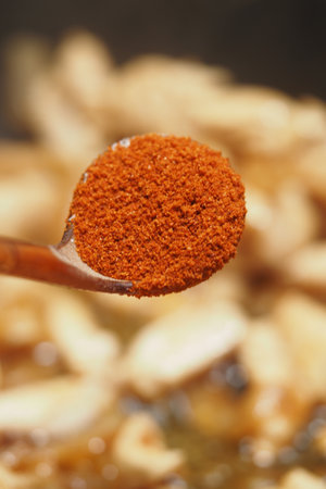 Spicy red powder on a spoon above a blurred cooking backgroundの写真素材