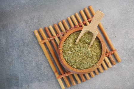Dried herbs arranged in bowl with wooden scoop on bamboo matの写真素材